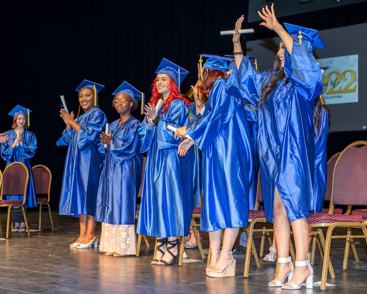 Edge High School student graduates in blue caps and gowns standing on a stage