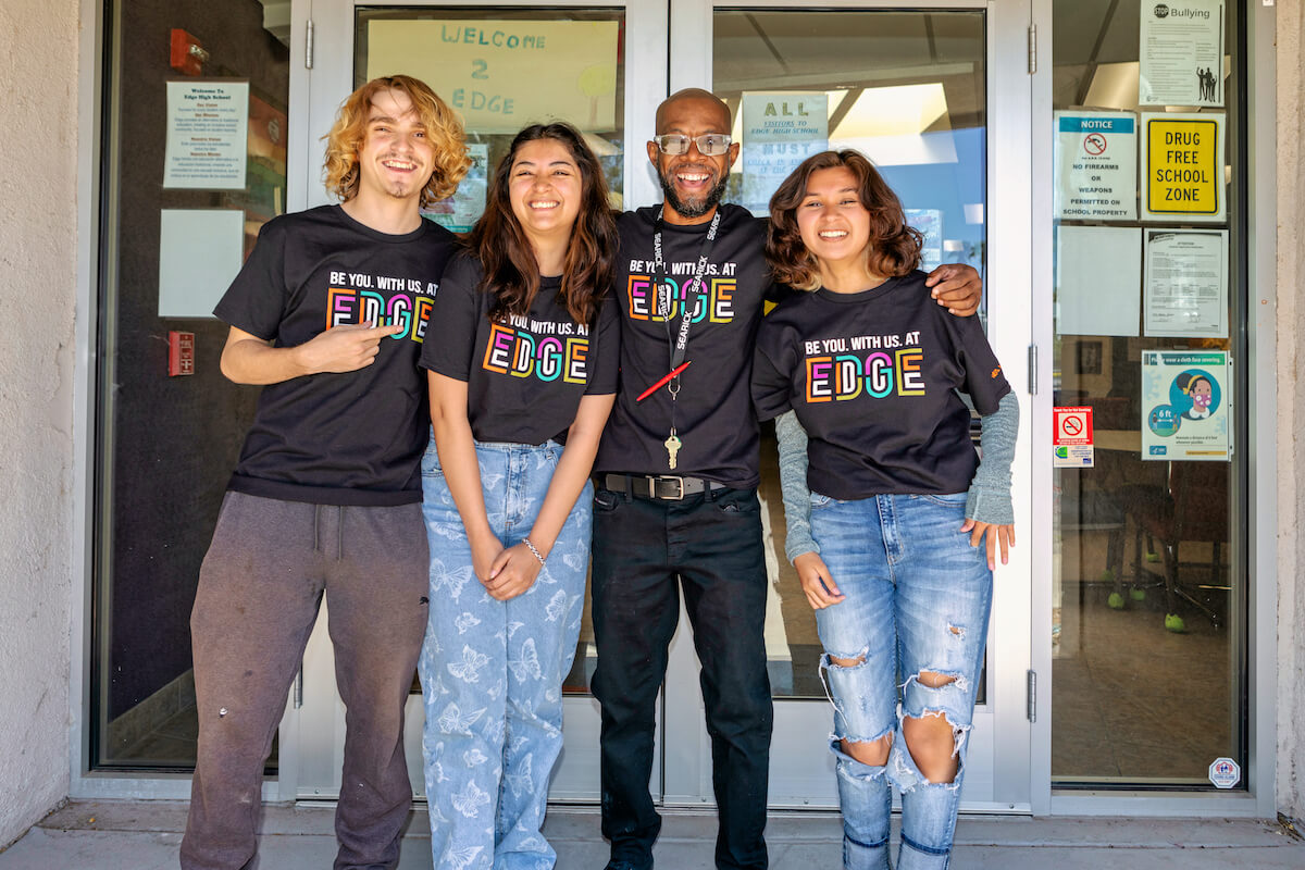Lo Sanders, counselor at tuition-free Edge High School, standing with arms around 3 smiling Edge students.